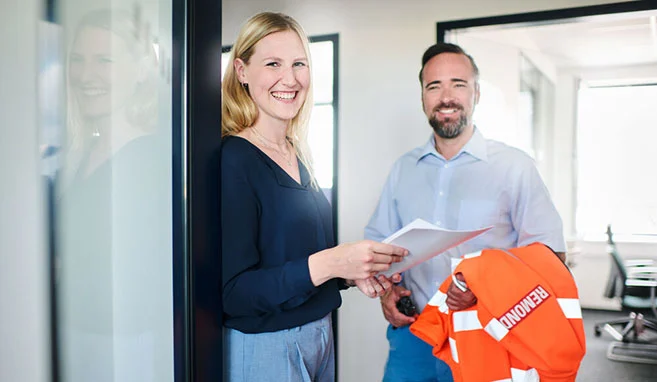 Zwei REMONDIS-Mitarbeitende stehen in einem Büro und lachen in die Kamera.