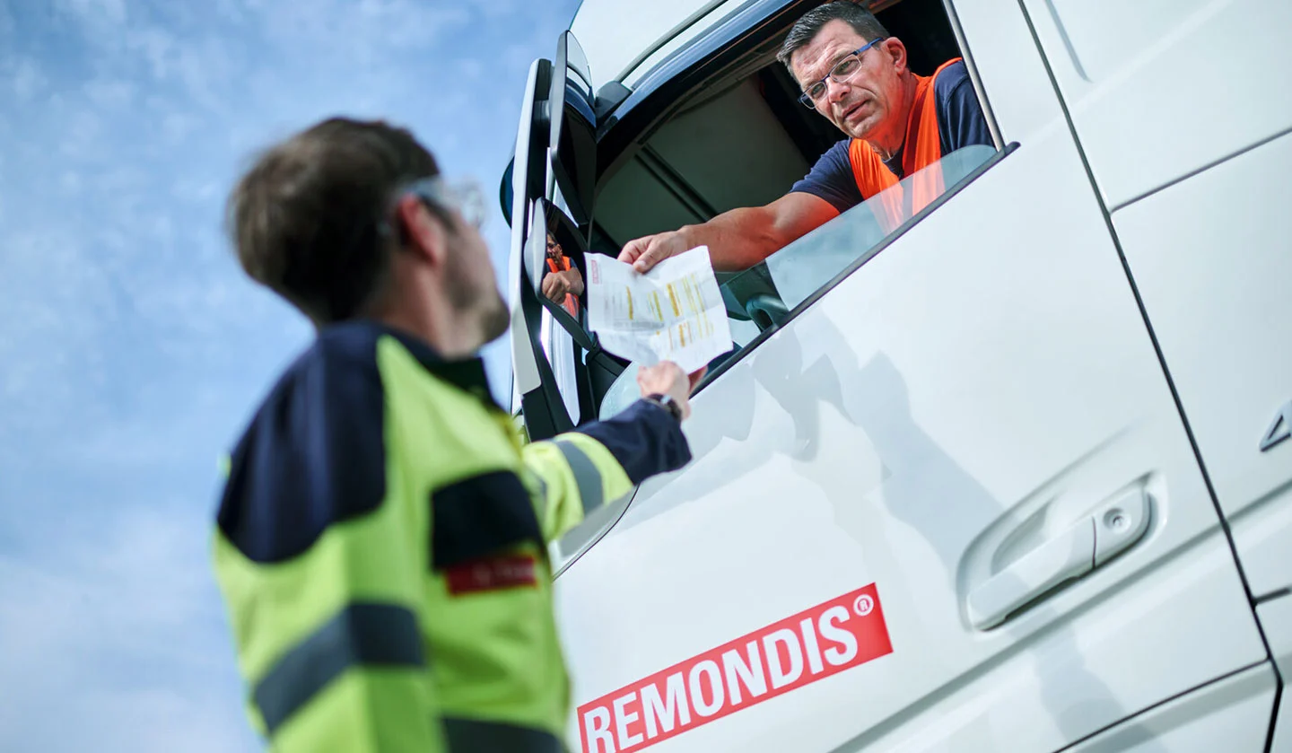 Ein Mitarbeiter gibt einem LKW-Fahrer von REMONDIS ein Datenblatt.
