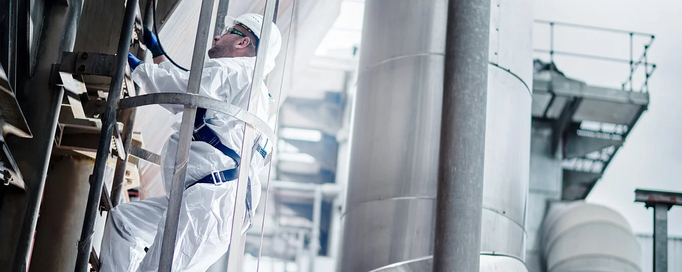 Mann in Schutzkleidung klettert eine Leiter in einer Industrieanlage hoch